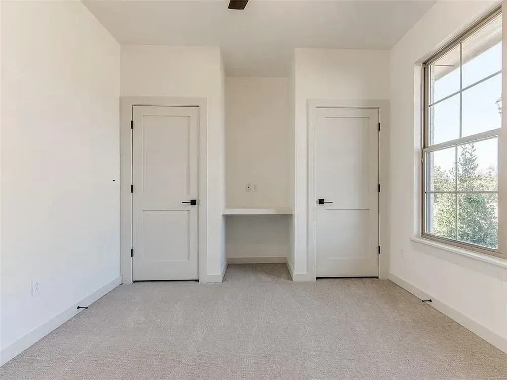 Empty room with two white doors, a small built-in desk, and a window to the right.