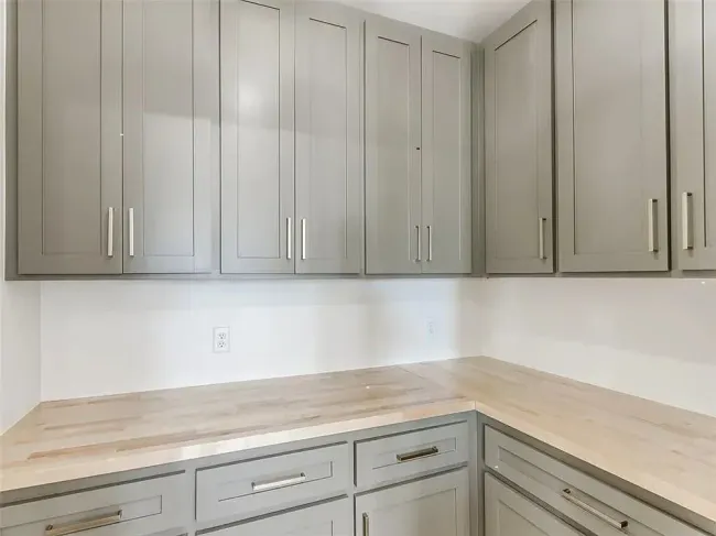 Gray kitchen cabinets with light wood countertops in a corner setting.