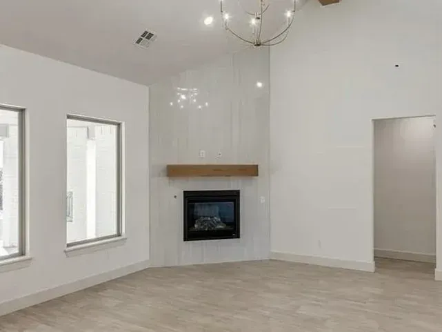 Empty living room with fireplace, high ceiling, and large windows.