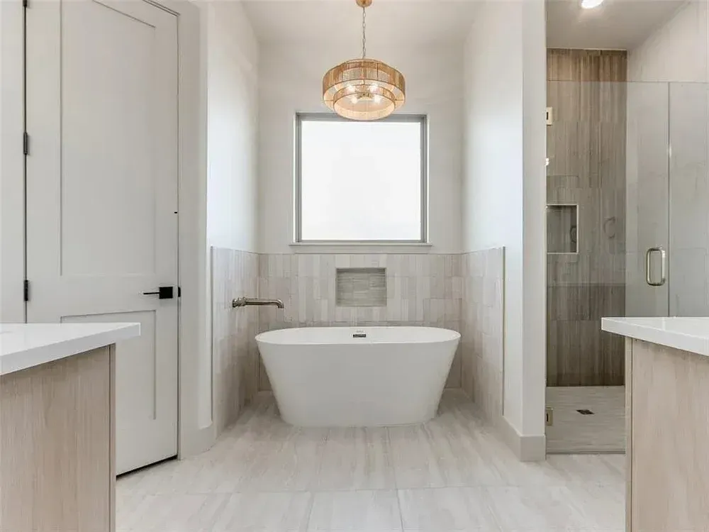 Bathroom with a white freestanding tub beneath a window and a gold light fixture.