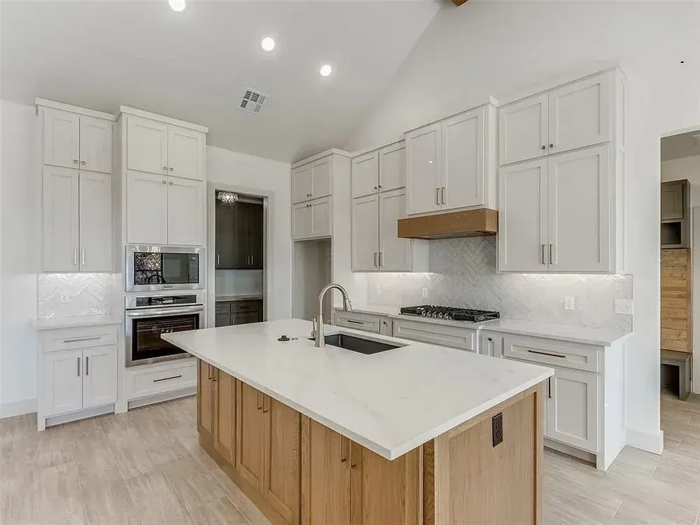 Modern kitchen with white cabinets, light wood island, and stainless steel appliances.