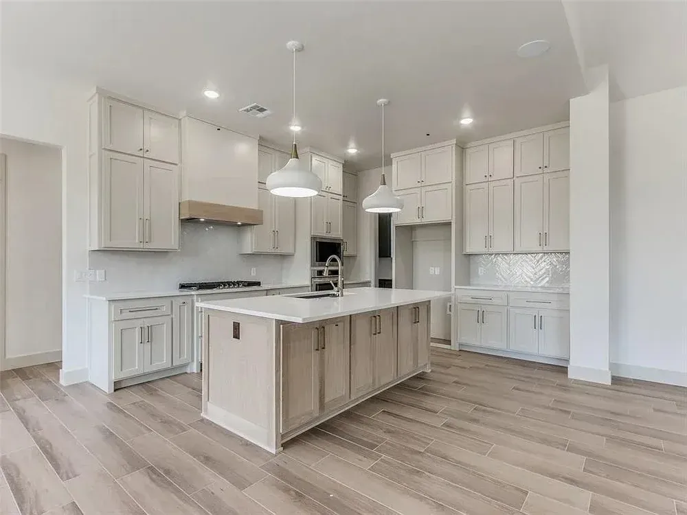 Spacious, light-filled kitchen with white cabinetry, central island, light wood floors, and pendant lighting.