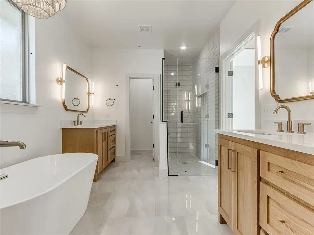 Spacious white bathroom with wooden vanities, freestanding tub, and glass shower; gold fixtures.
