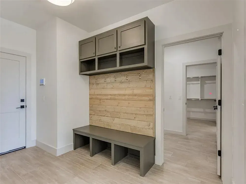 A gray mudroom entryway with bench, cabinets, and light wood wall paneling. A white door is visible.
