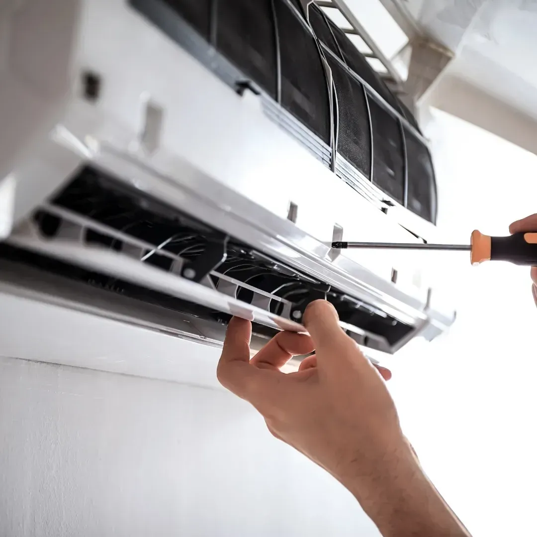 Hands using a screwdriver to clean or repair an air conditioner indoors