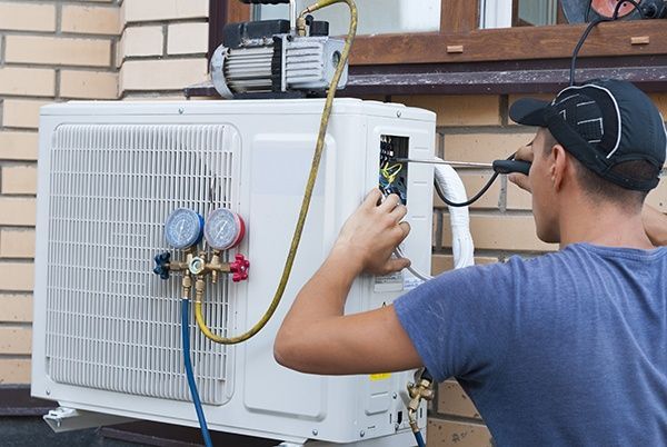 A technician installs an outdoor air conditioning unit, using a vacuum pump.