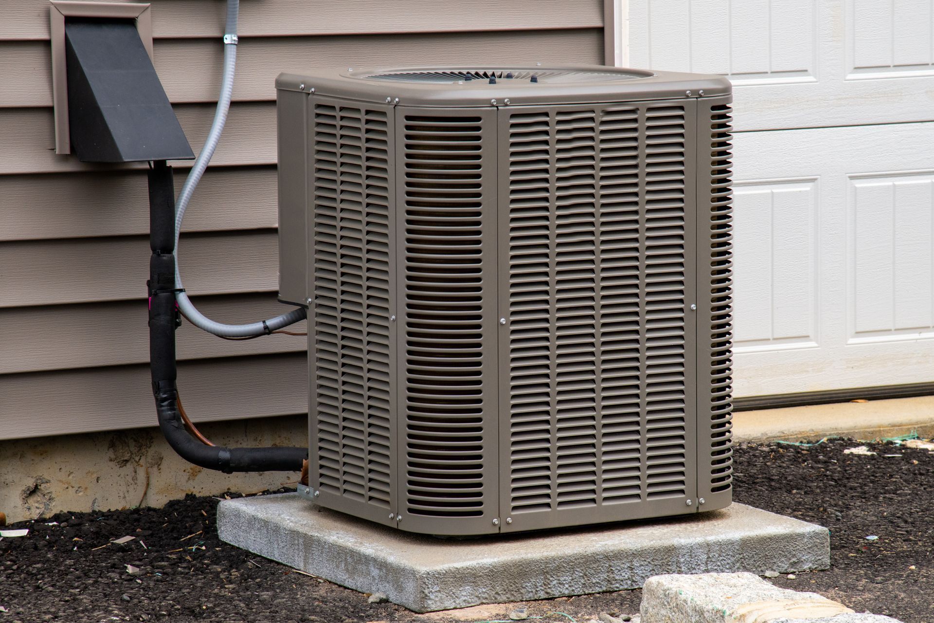 An outdoor central air conditioning unit resting on a concrete pad against the tan siding of a house.