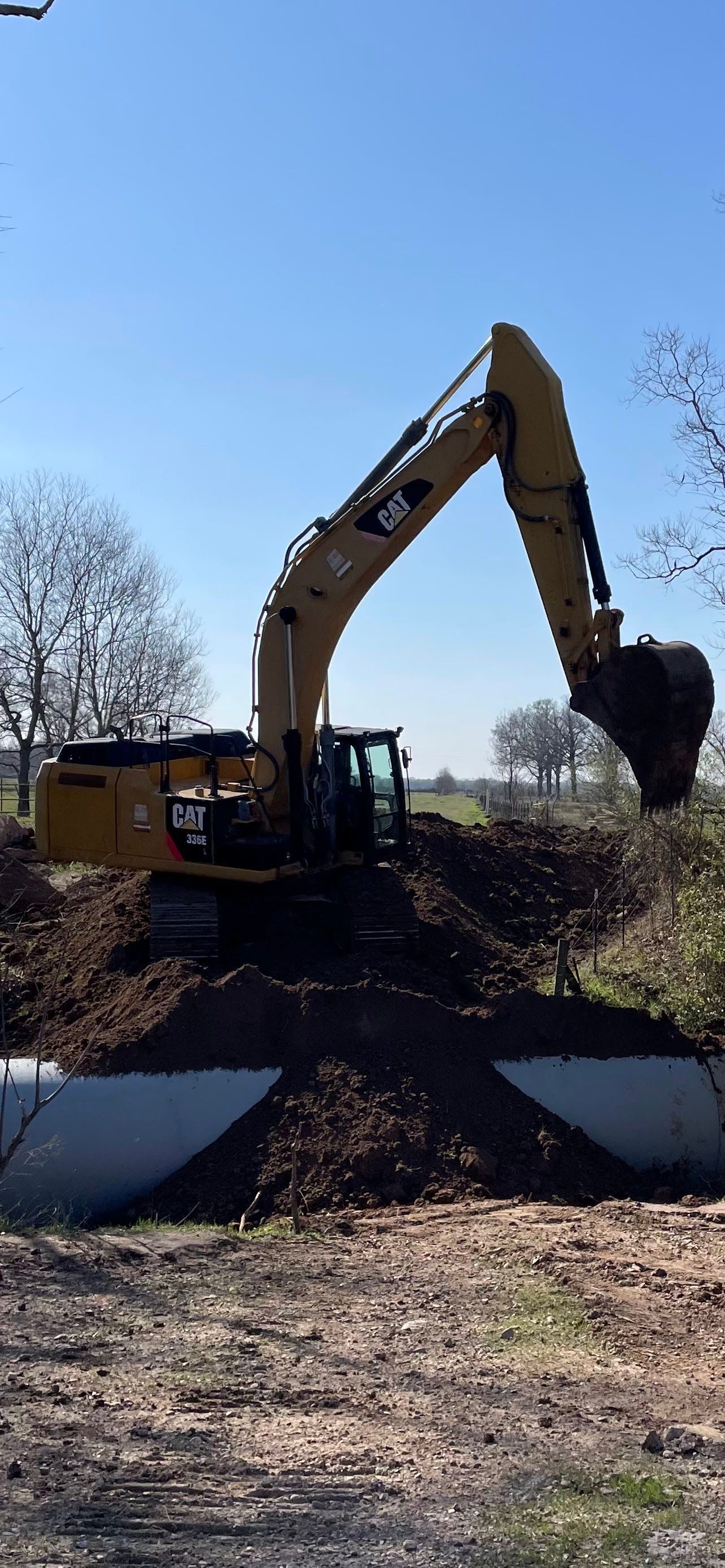 Yellow excavator digging in dirt, sunset sky.