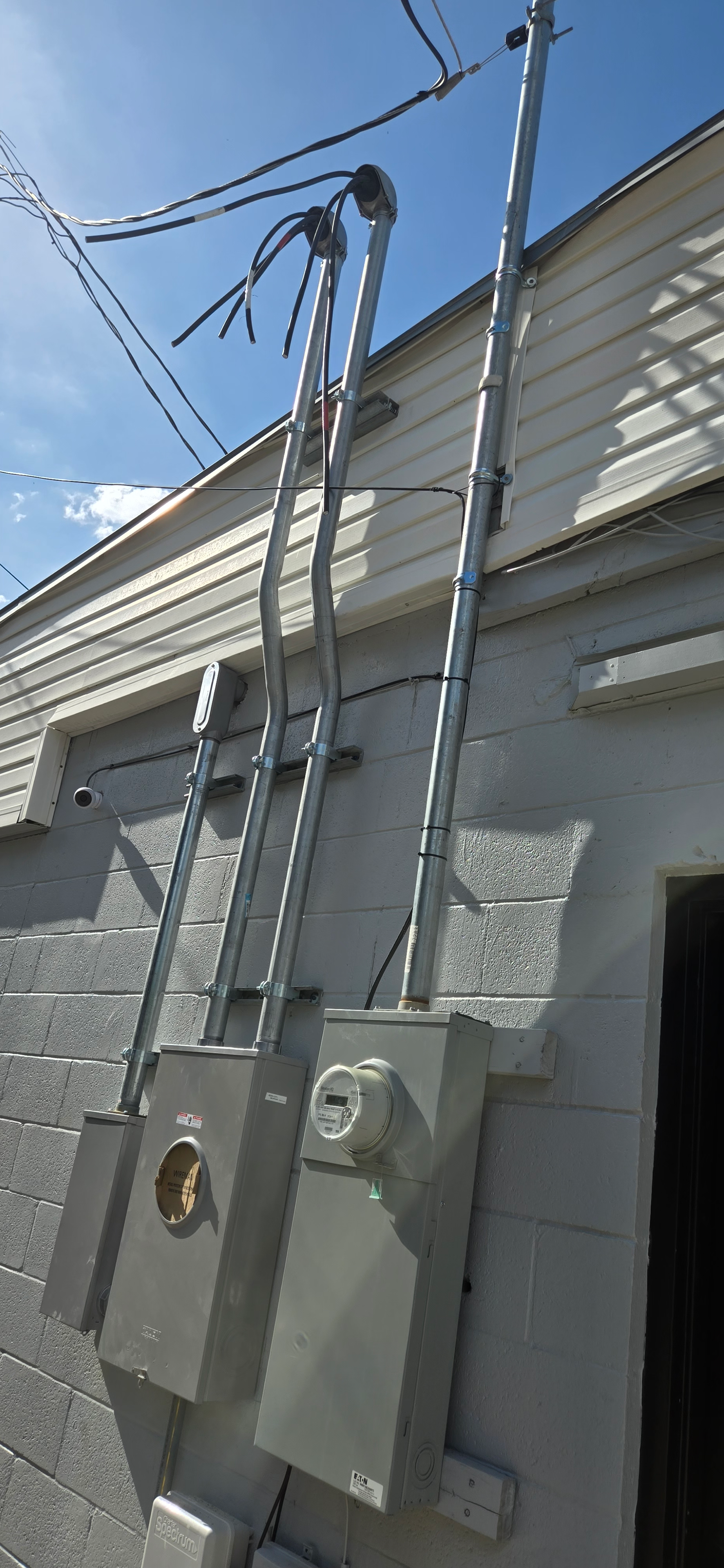 Utility meters and cables mounted on an exterior wall beside a doorway under a blue sky