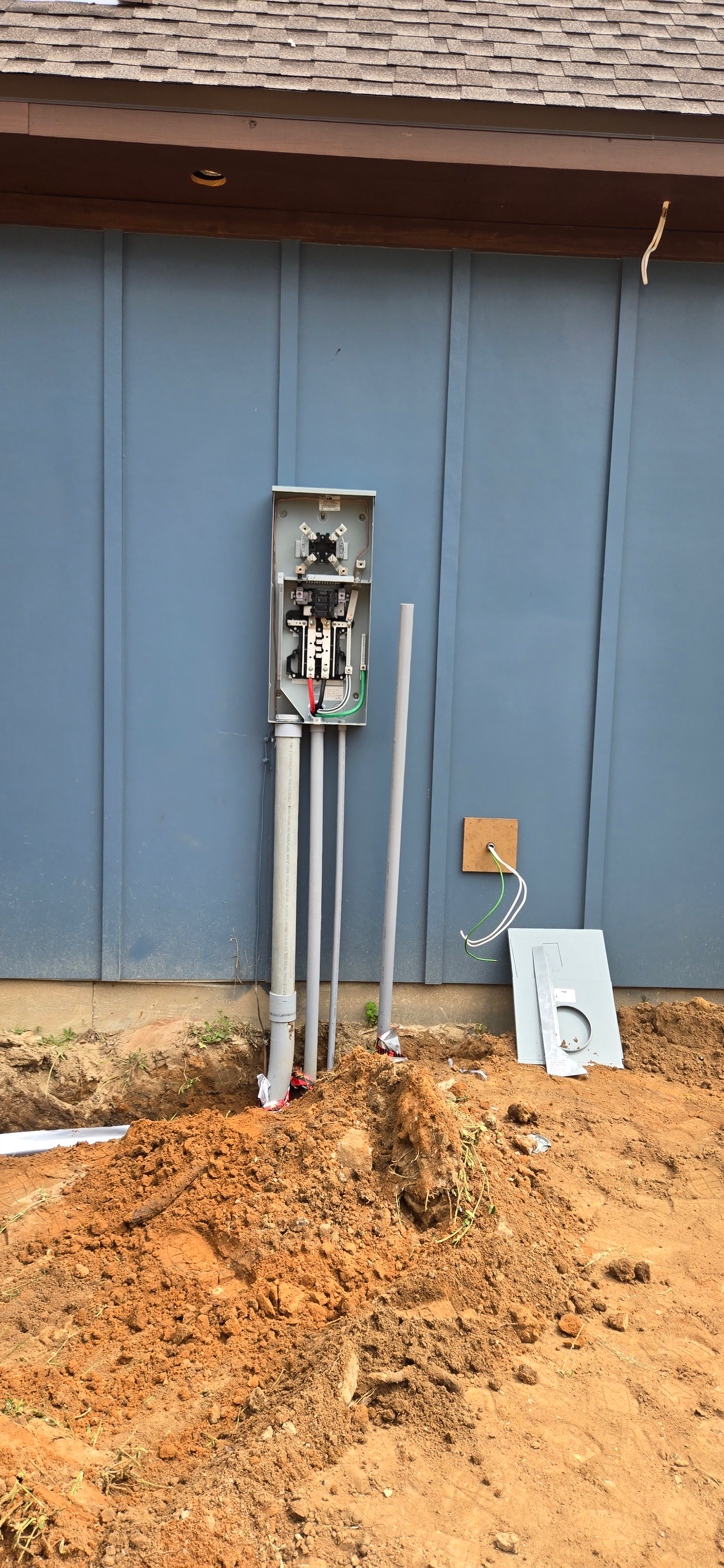 Electric meter and conduit mounted on a blue exterior wall beside a dirt trench.