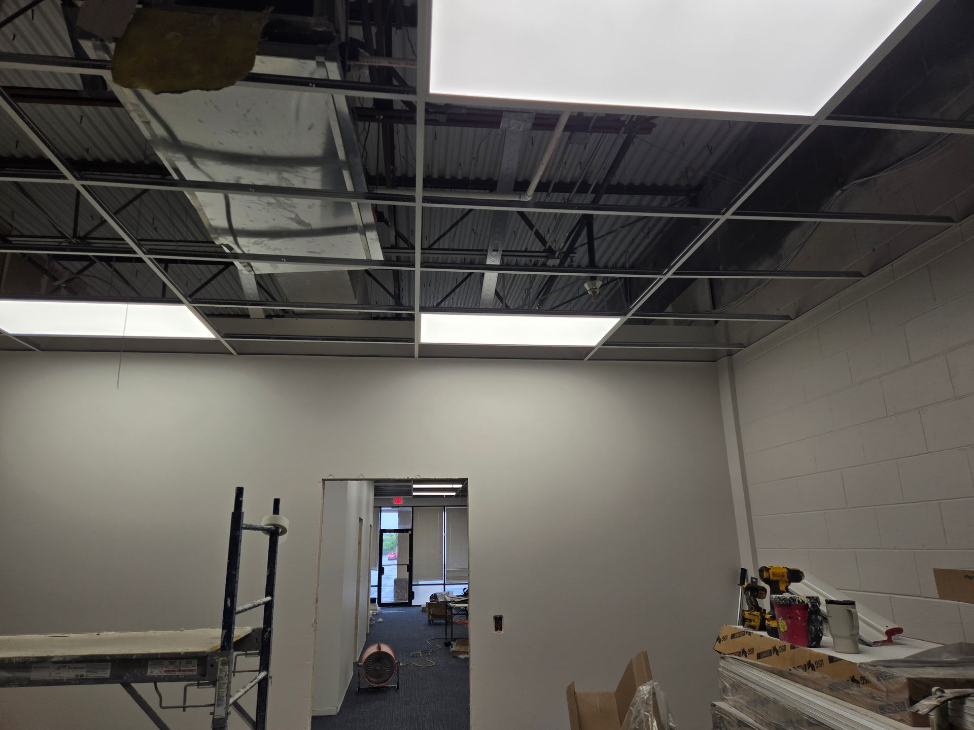 Partially finished room with exposed ceiling, white walls, and a doorway to a lit office corridor