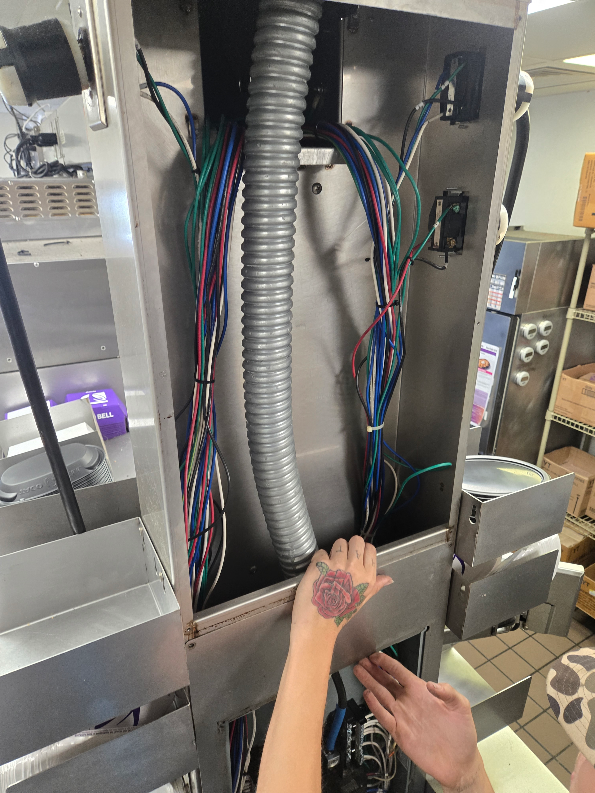 Hands wiring a metal electrical cabinet with multicolored cables and a gray conduit.