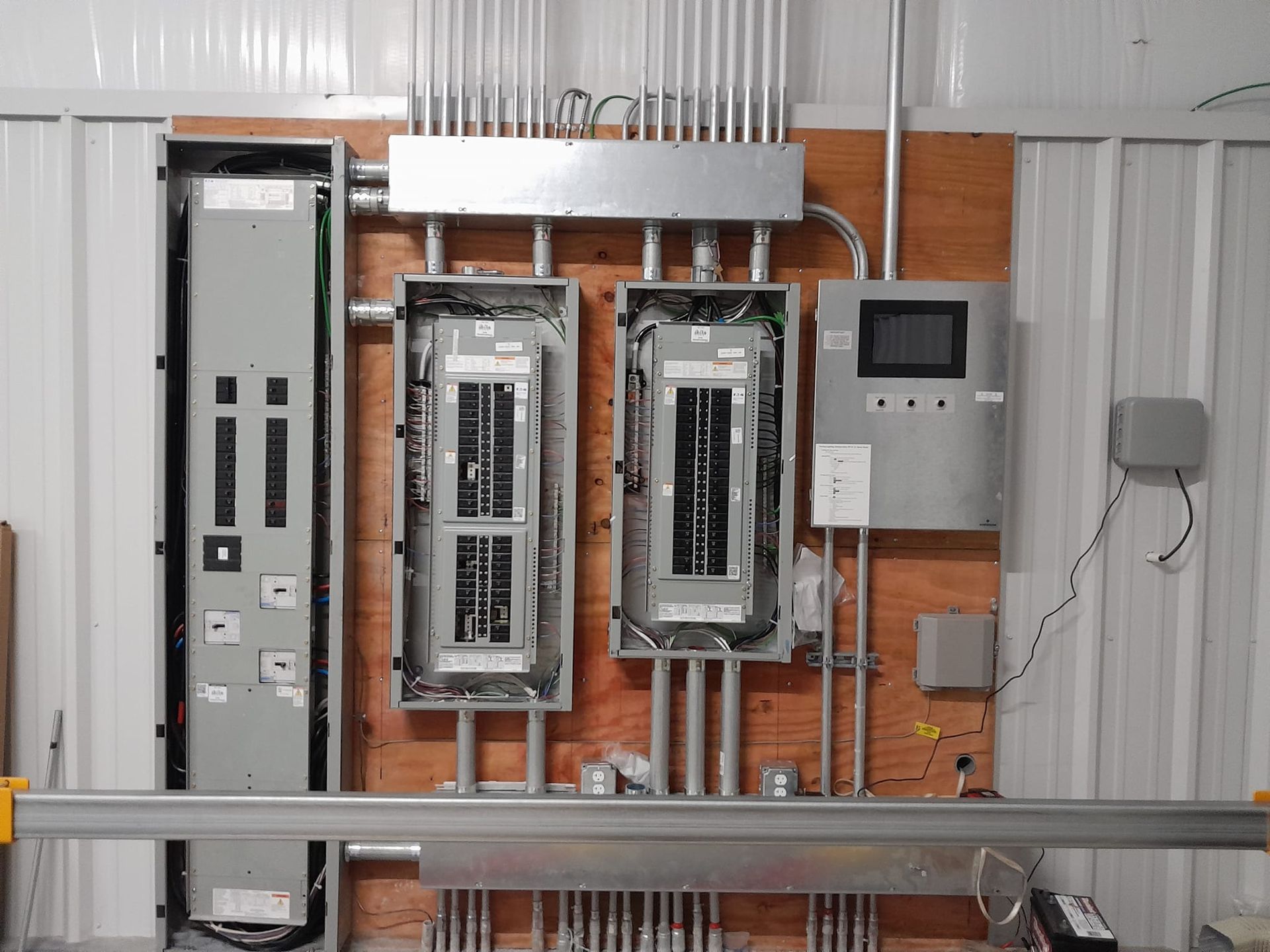 An industrial electrical panel setup with four gray utility boxes and conduit piping mounted on a plywood wall.
