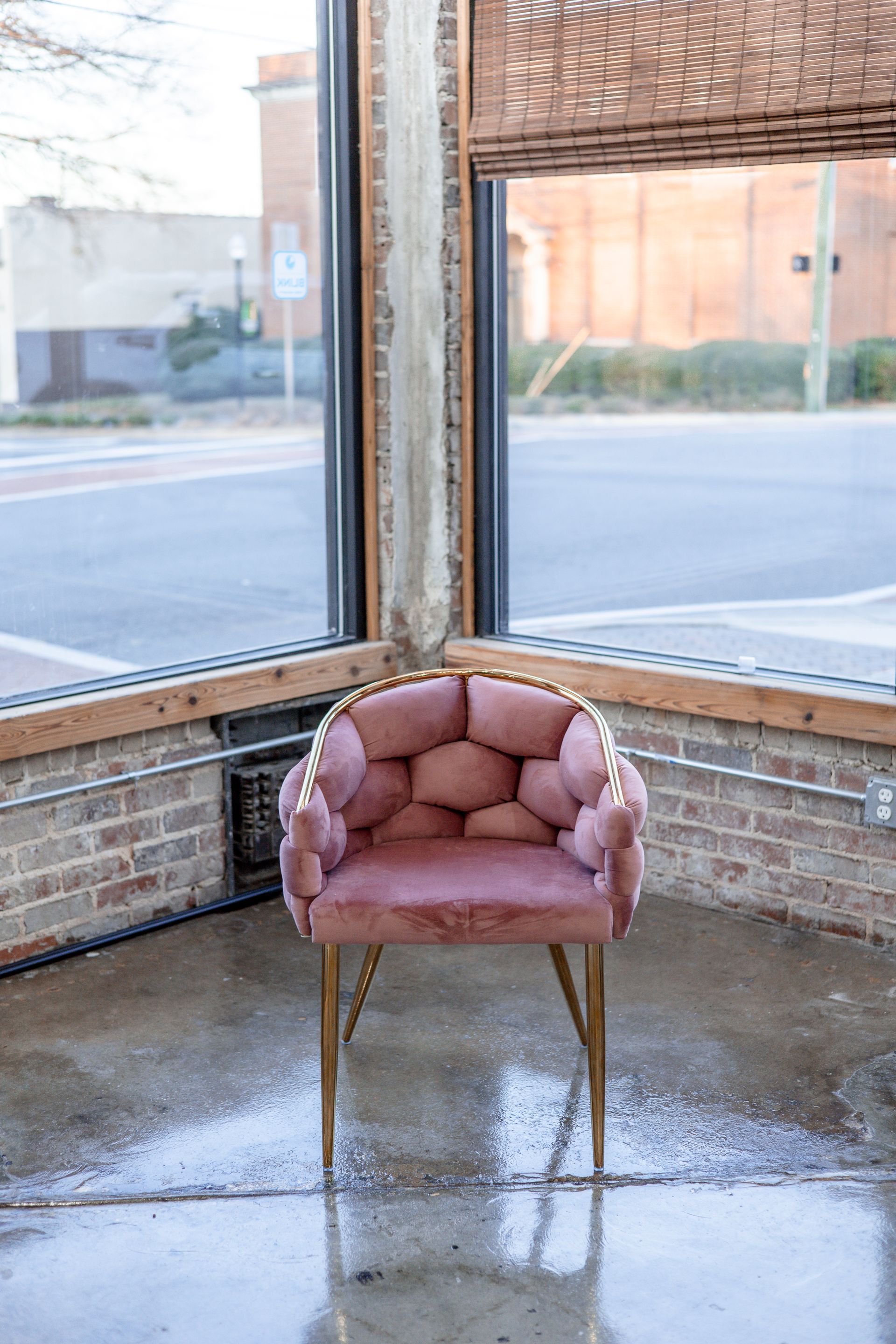 Pink velvet chair with gold trim, in front of a window.