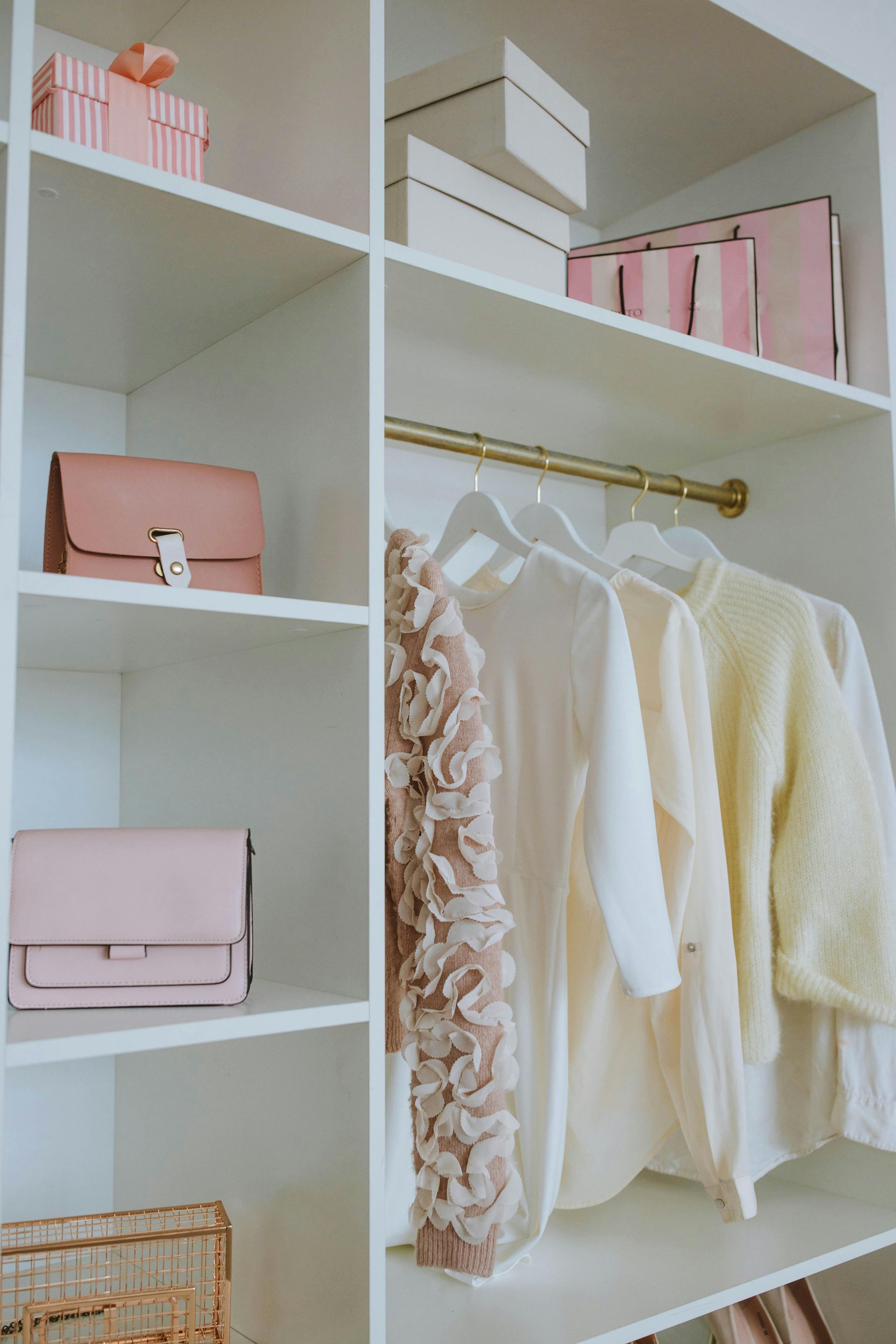 White closet with pastel-colored purses, boxes, and clothing on hangers.