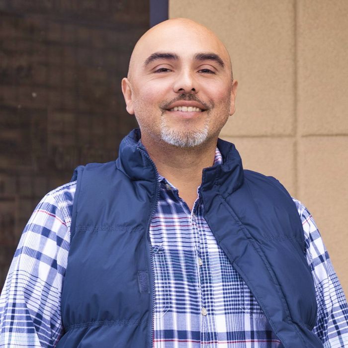 A man wearing a plaid shirt and a blue vest smiles for the camera