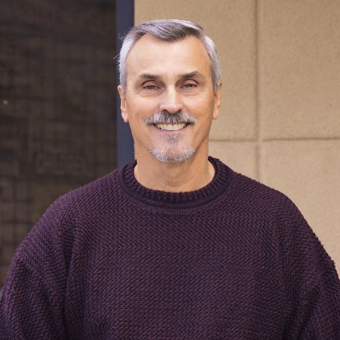 A man with a beard is wearing a purple sweater and smiling.