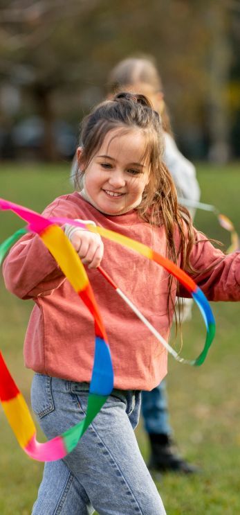 A little girl is playing with a colorful ribbon in a park.