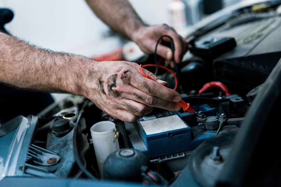 Hands using jumper cables to start a car engine in a garage