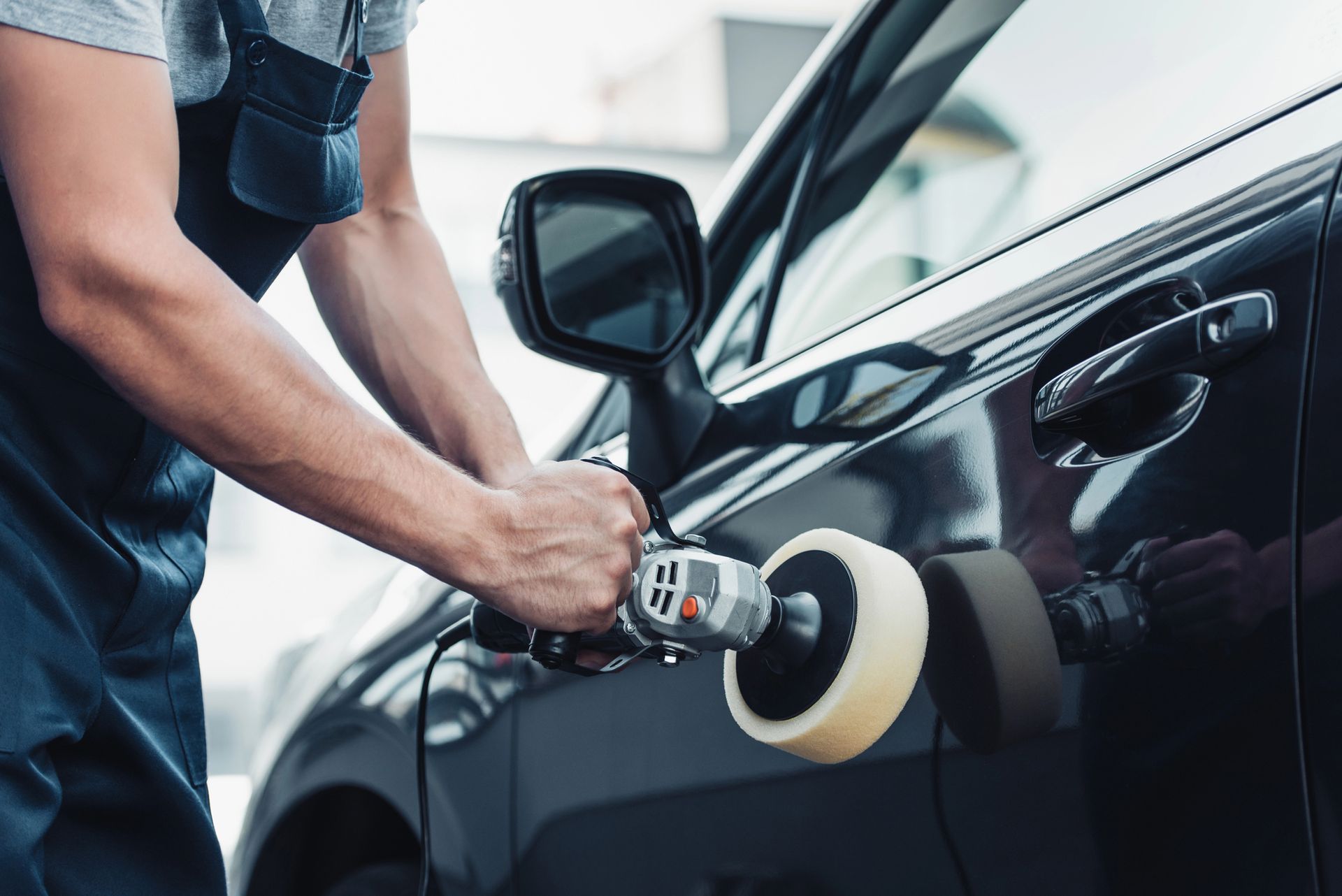 Person using a buffer to polish a black car door at a car wash