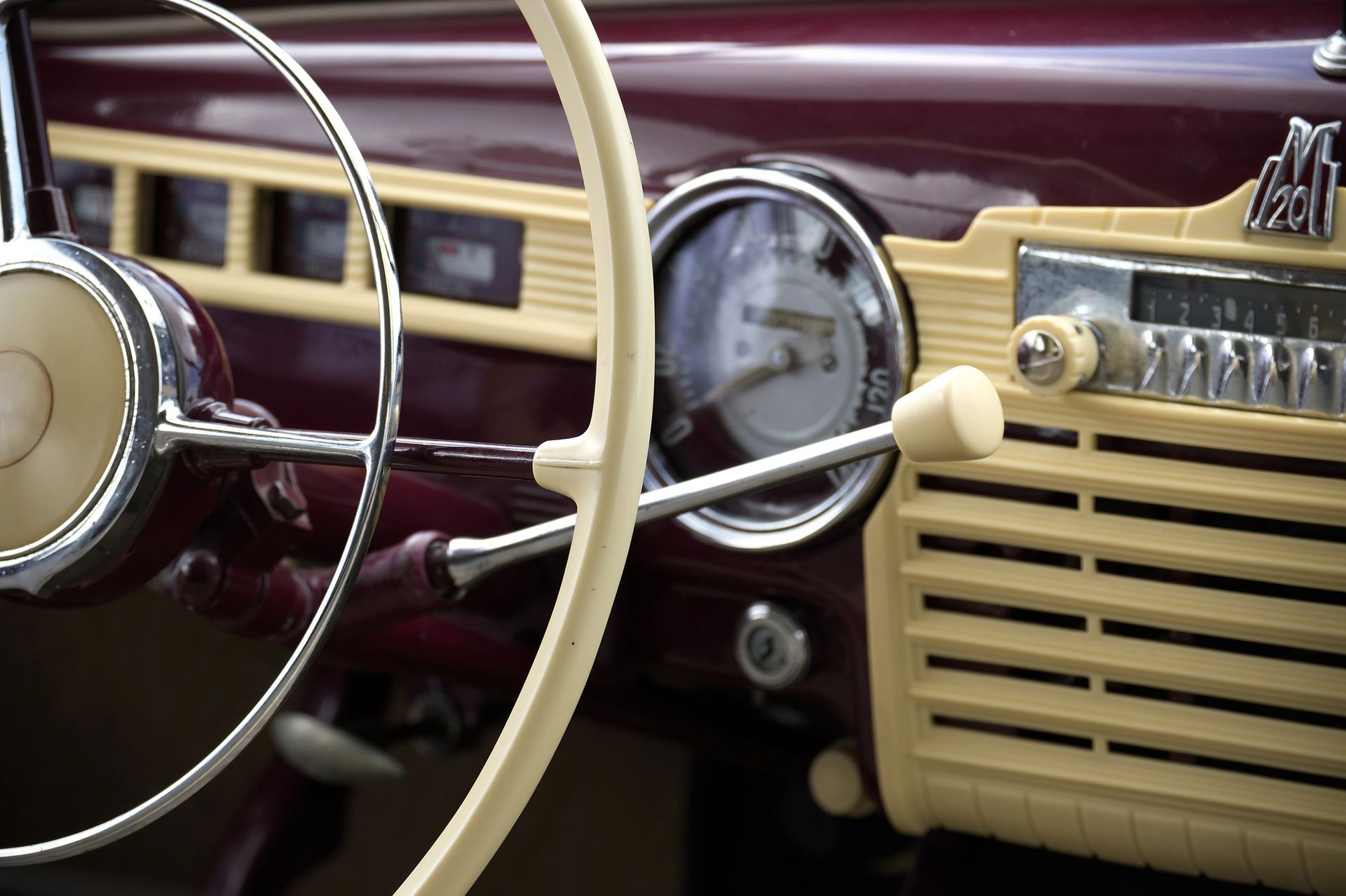 Close-up of a vintage car dashboard with cream steering wheel, chrome gauges, and maroon interior