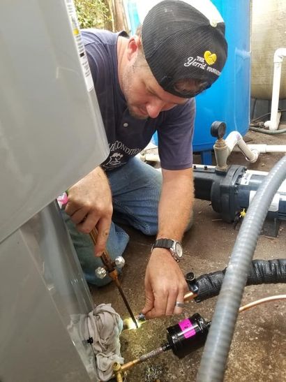 Worker crouches beside equipment, adjusting a hose and fittings near a tank and pump.