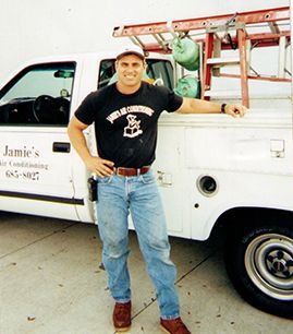 Man leaning on a white utility truck with ladder and green tanks, smiling outdoors