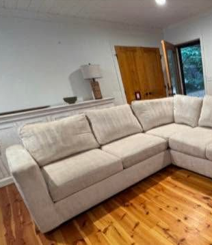 Beige sectional sofa in a bright living room with wooden floors and a door open to outside.