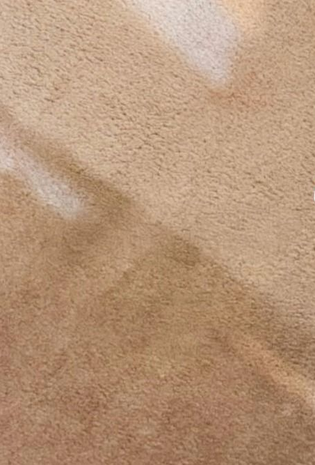 Close-up of a beige and tan textured fabric surface with a diagonal seam and light reflections