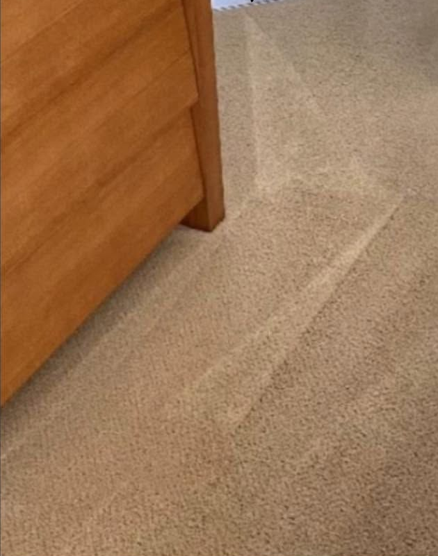Close-up of a beige carpet next to a wooden dresser leg and side panel.