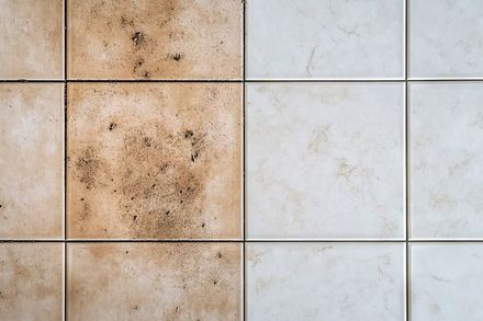 Dirty beige and white tiled wall with stained grout and rust-like marks
