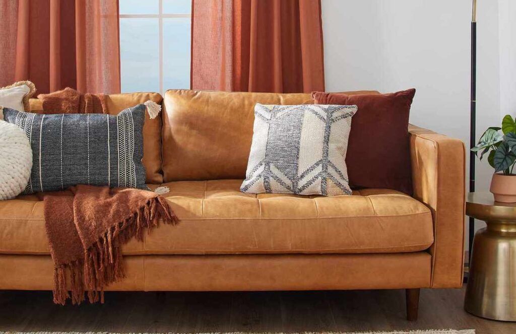 Cozy living room sofa with brown and gray pillows, a rust throw, and a small side table nearby