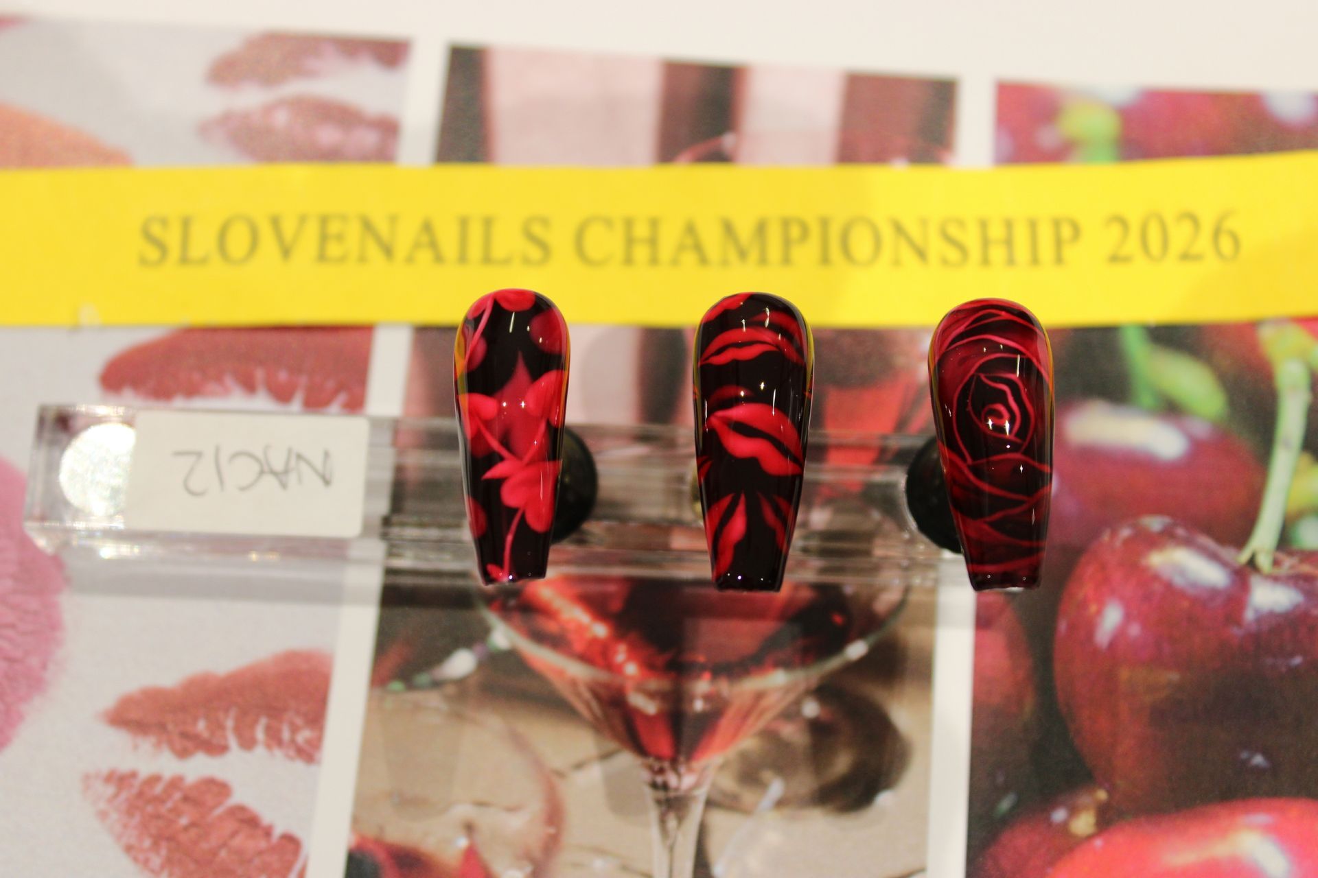 Three red-and-black decorated nail tips on a display labeled “SLOVENAILS CHAMPIONSHIP 2026”