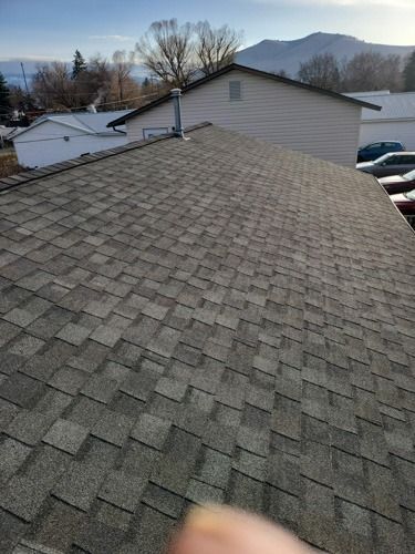 A person is pointing at the roof of a house with mountains in the background.