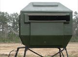 A green deer blind is sitting in the middle of a field.