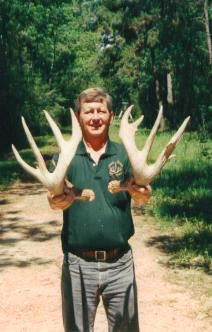 A man in a green shirt is holding two deer antlers in his hands.