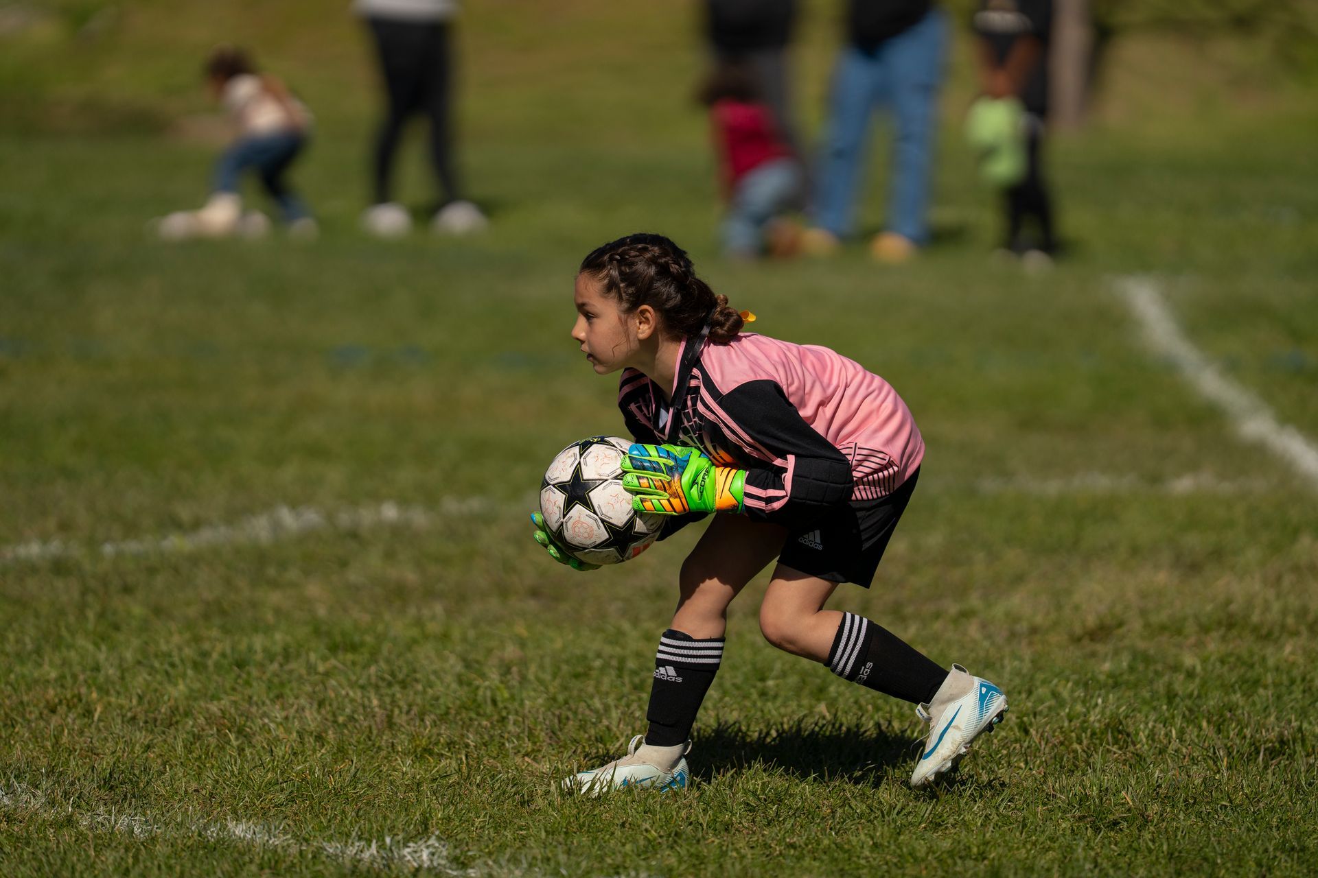 Young soccer player in pink and black jersey, holding a ball on the field.
