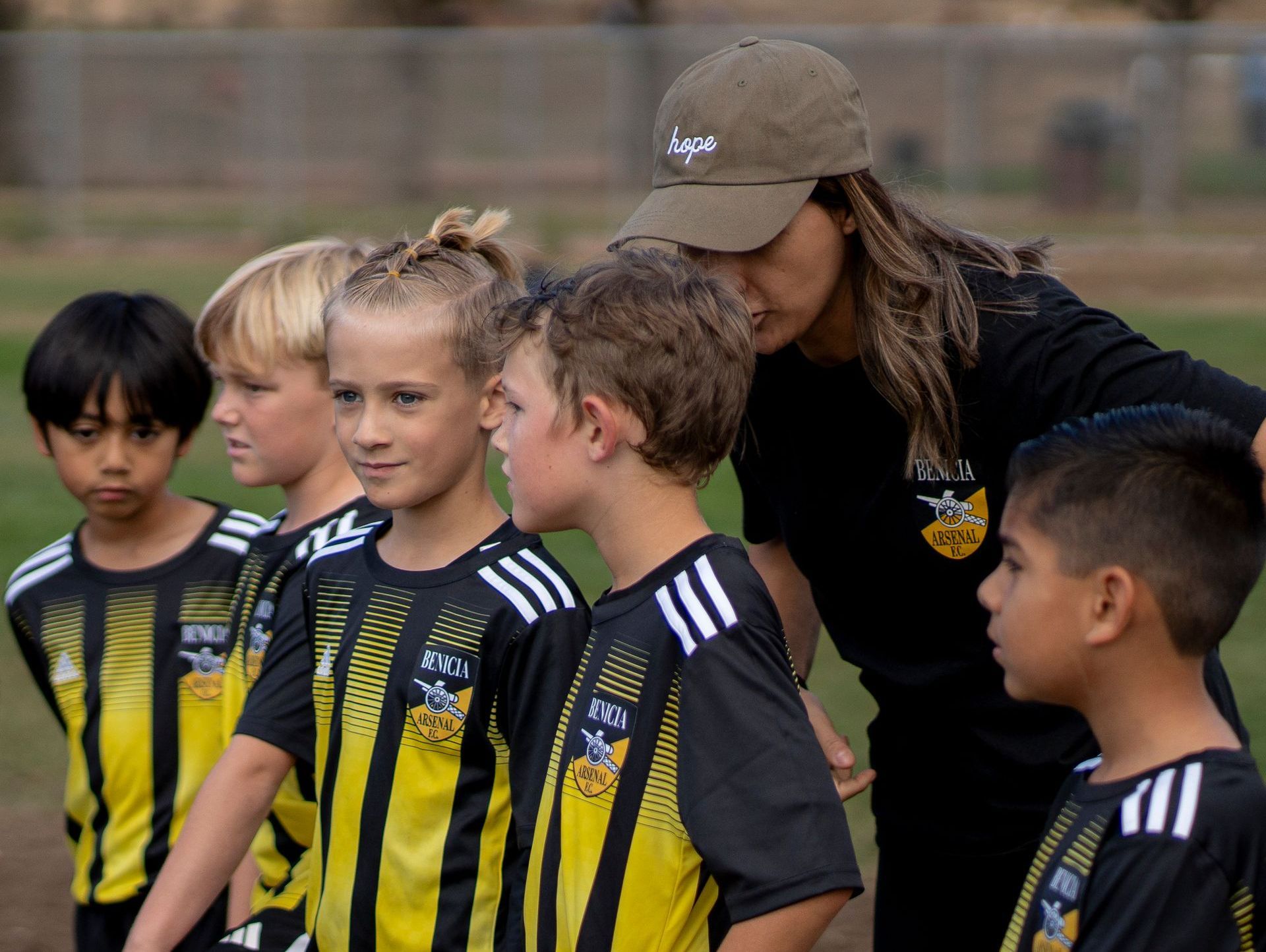Soccer coach with young players on a field, wearing black and yellow jerseys.