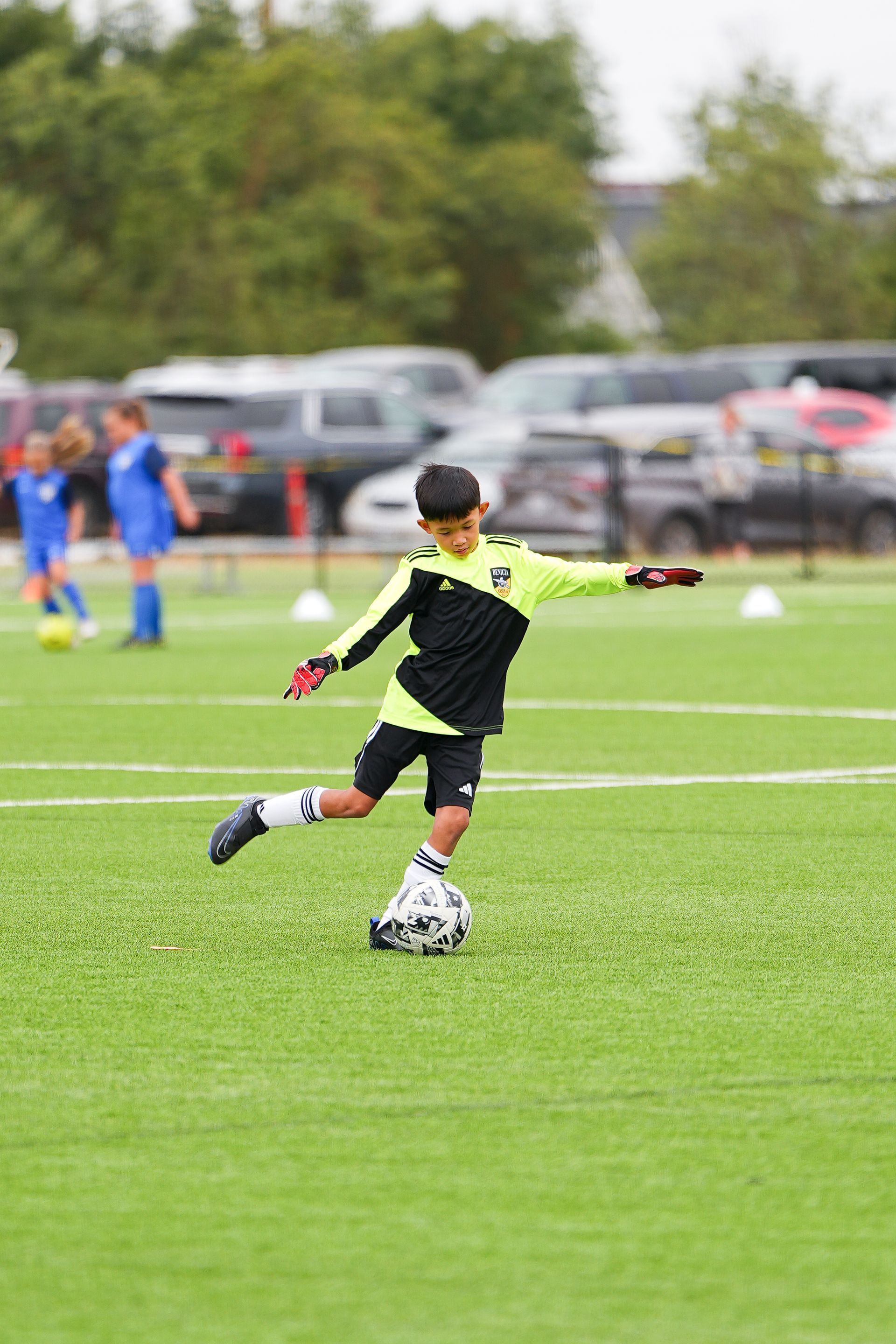 Boy in black and neon soccer uniform kicking ball on green field.