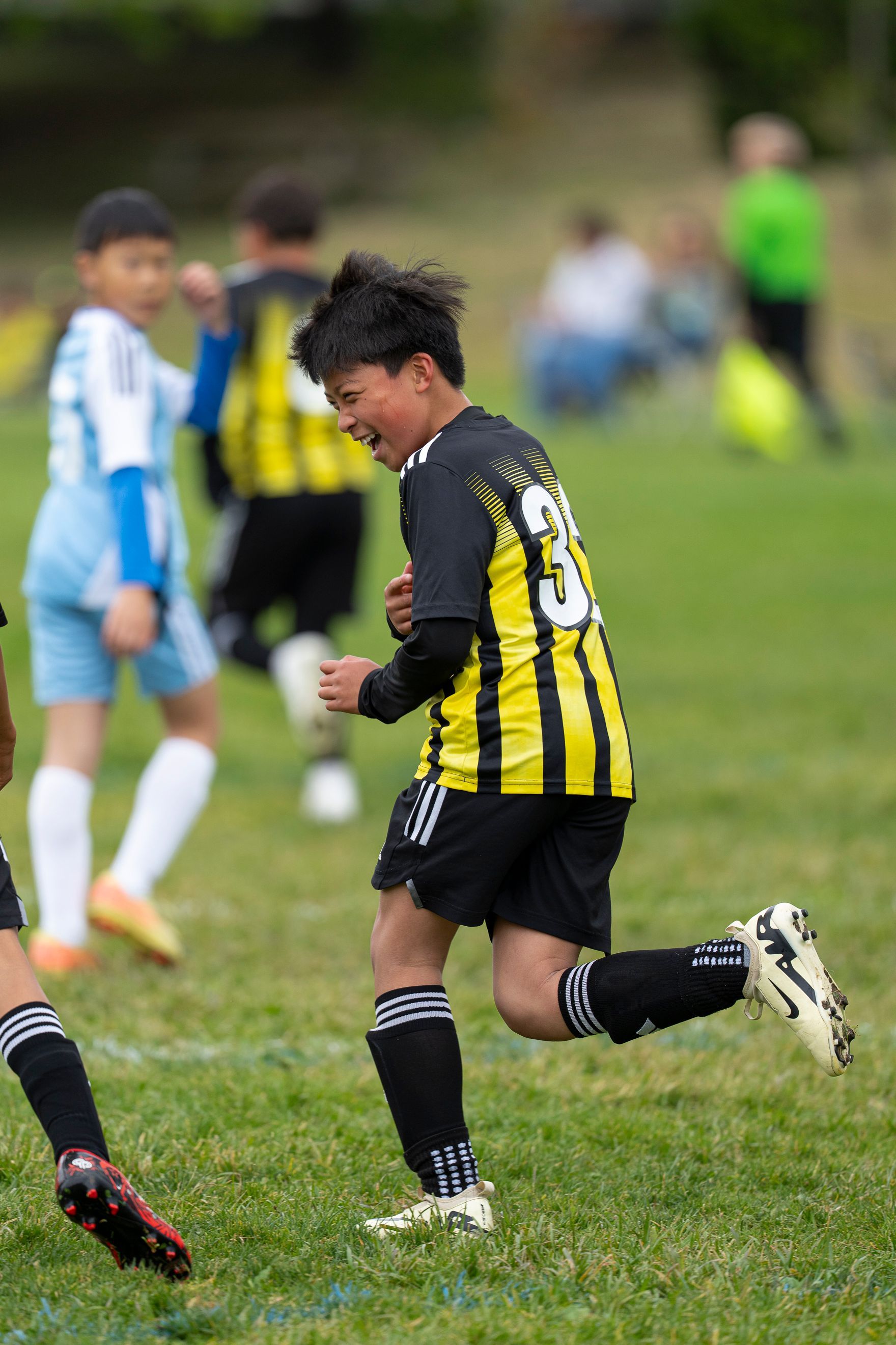 Soccer player in yellow and black jersey celebrating on field, running with arms up.