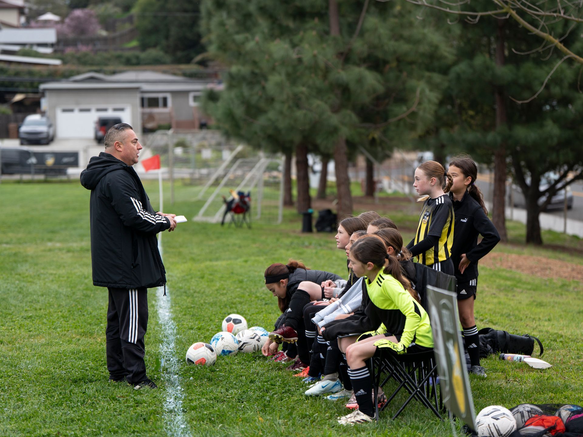 Soccer coach instructing a team on a grassy field; players seated, listening.