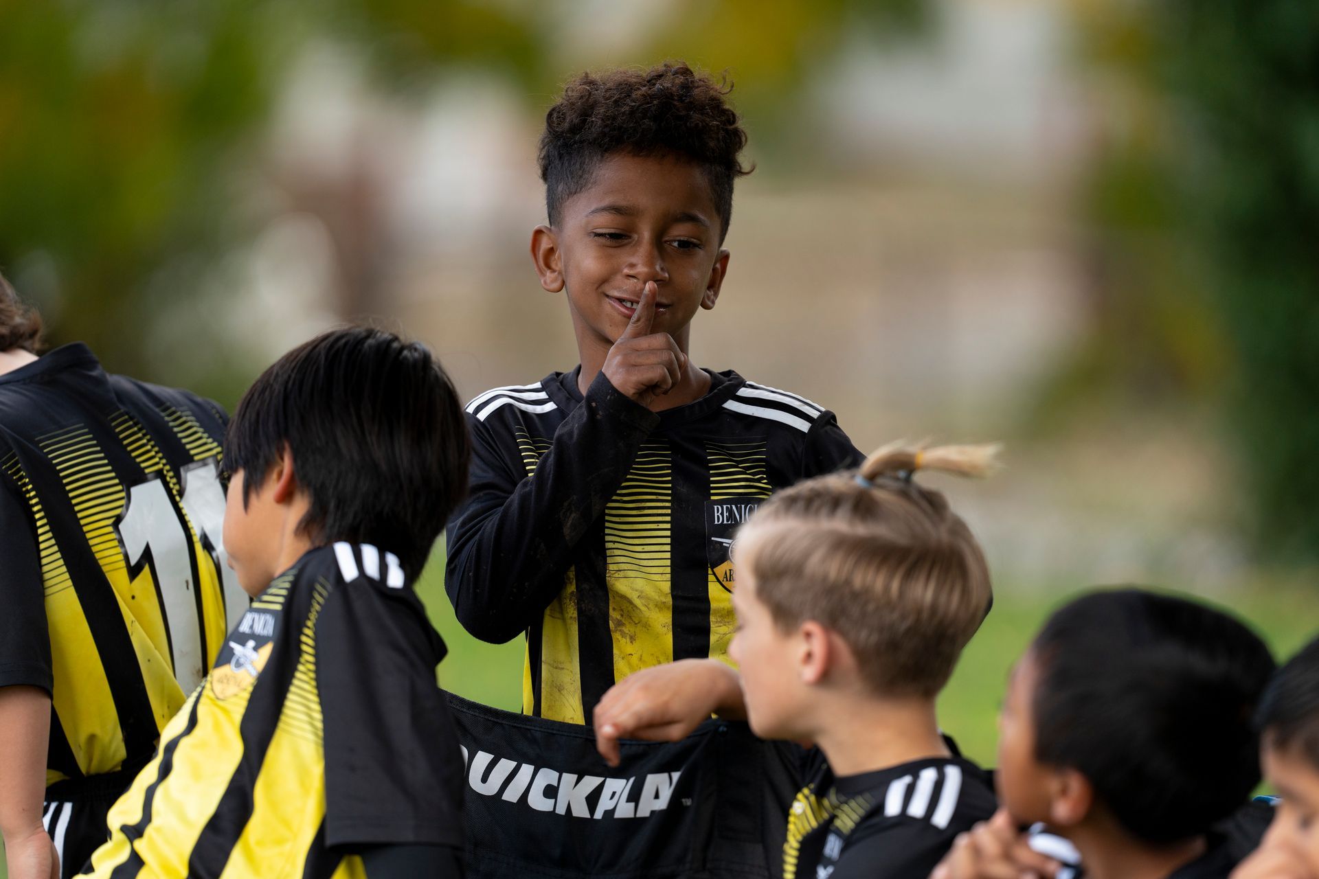 Boy on soccer team with finger to lips, surrounded by teammates.