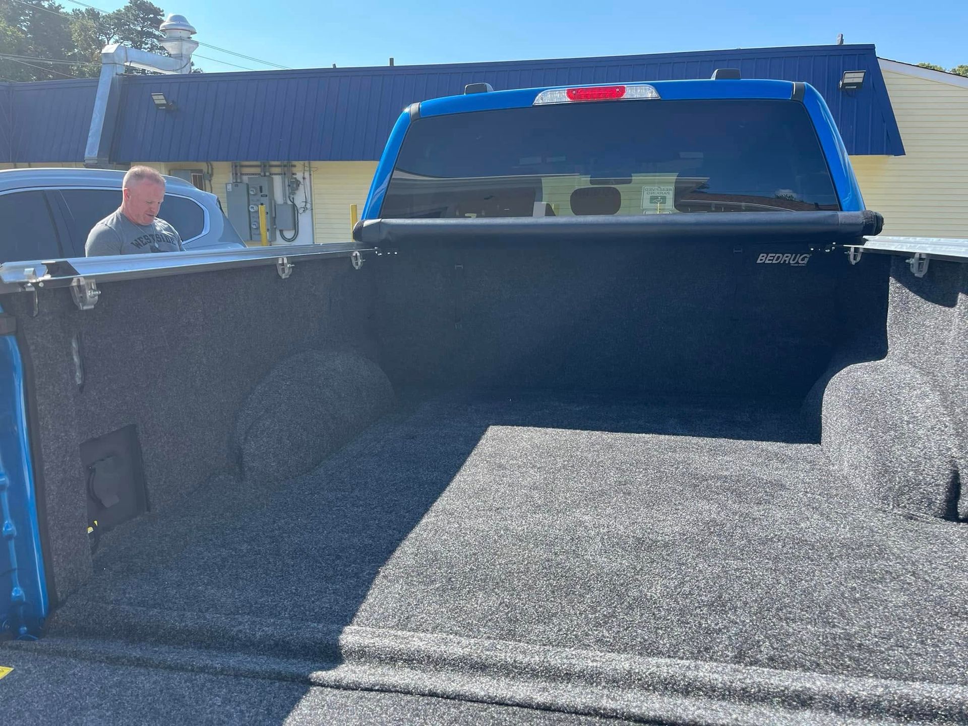 Blue pickup truck bed with a black cover; a person stands nearby.