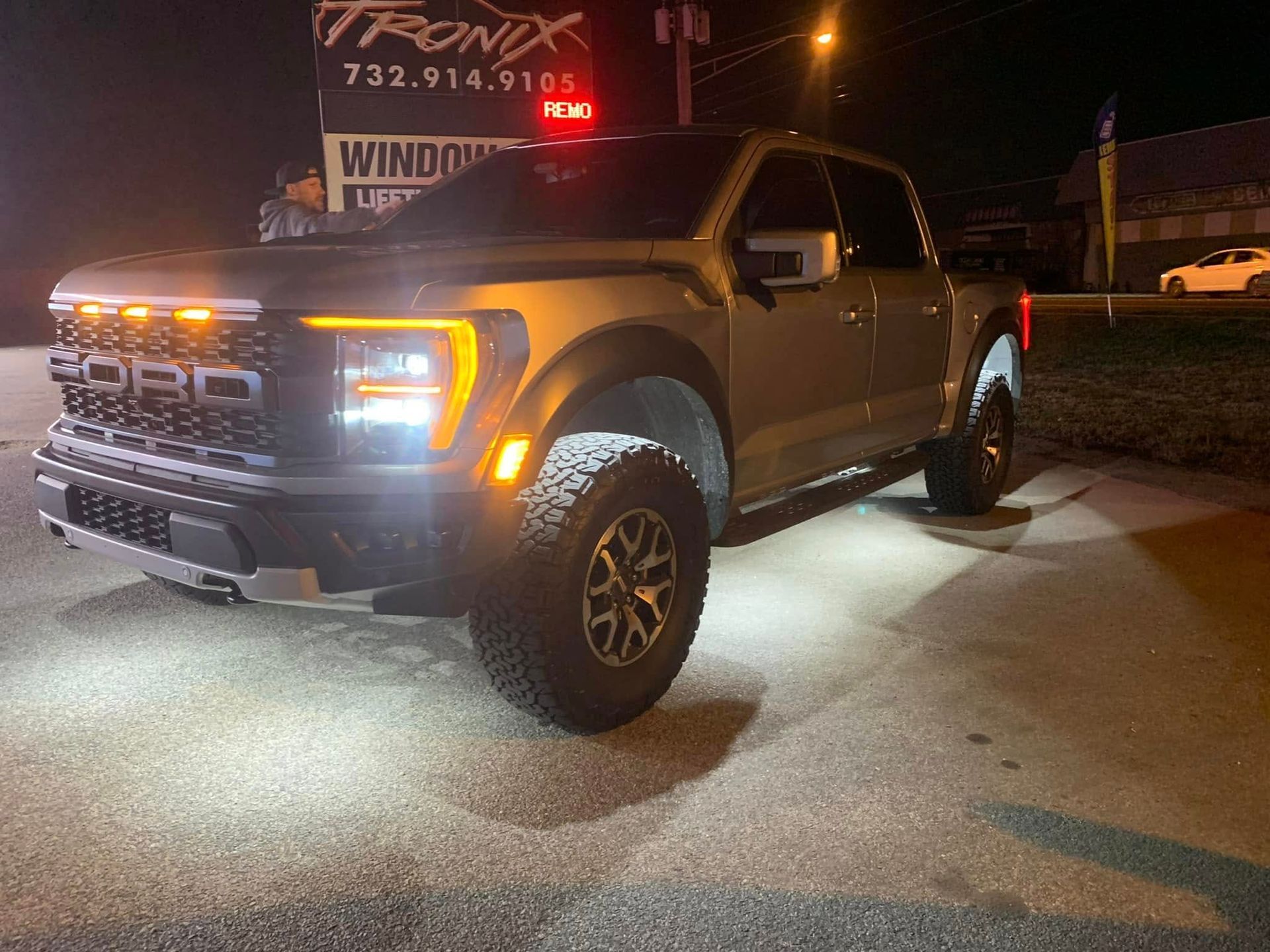 Ford Raptor truck parked at night, illuminated by lights.