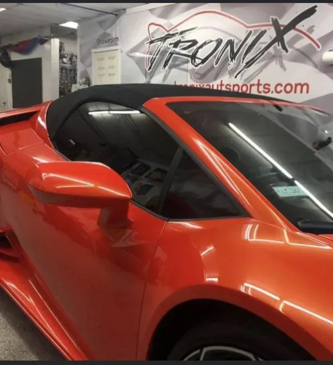 Orange convertible car with black top, parked inside a garage.