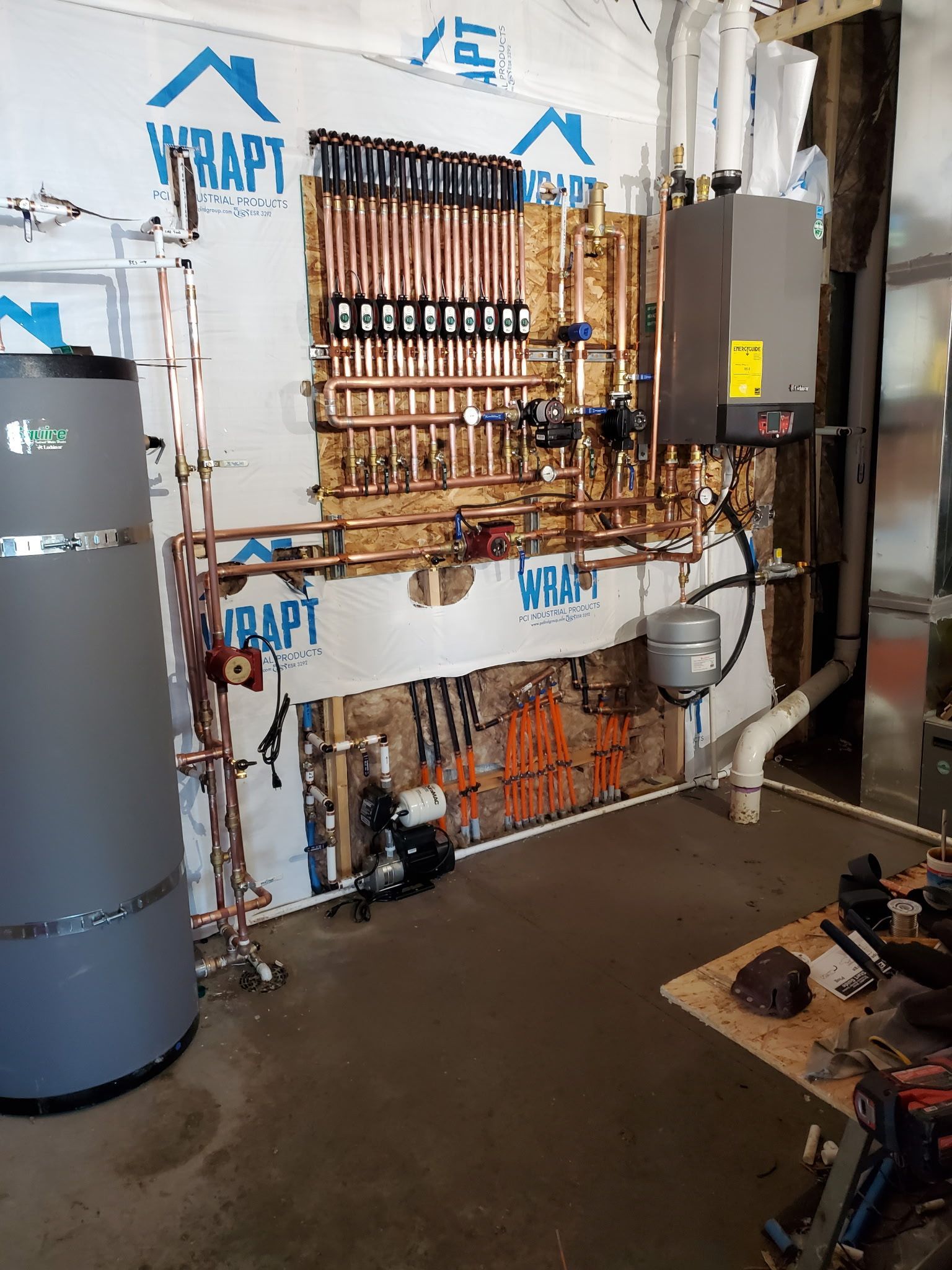 Plumbing system installed on a wall, featuring copper pipes, boiler, and water heater, in a construction setting.