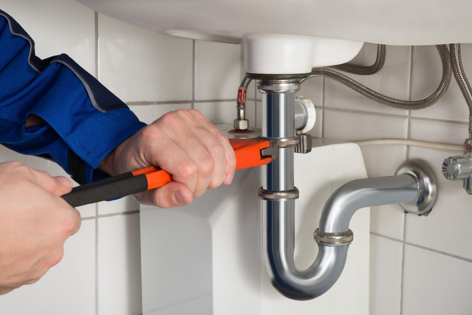 Plumber using a wrench to work on a sink's pipes.
