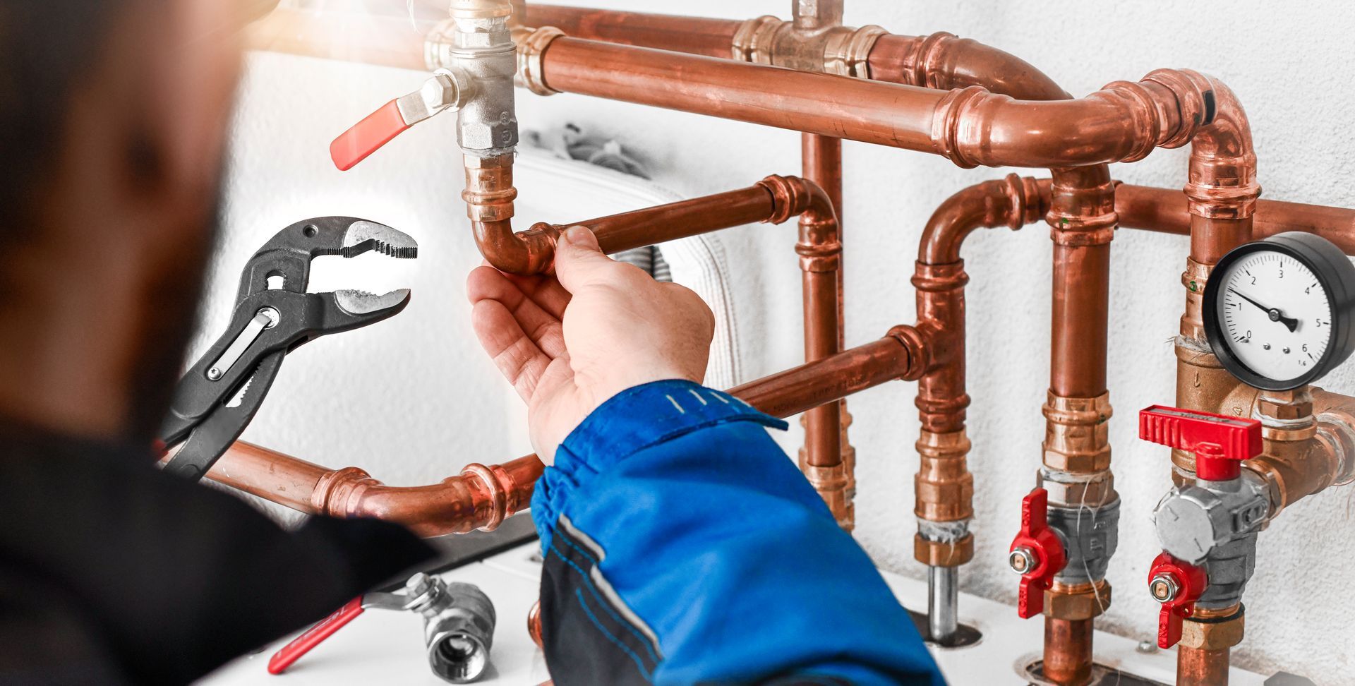 Plumber working on copper pipes with a wrench, valves, and a gauge in a utility room.