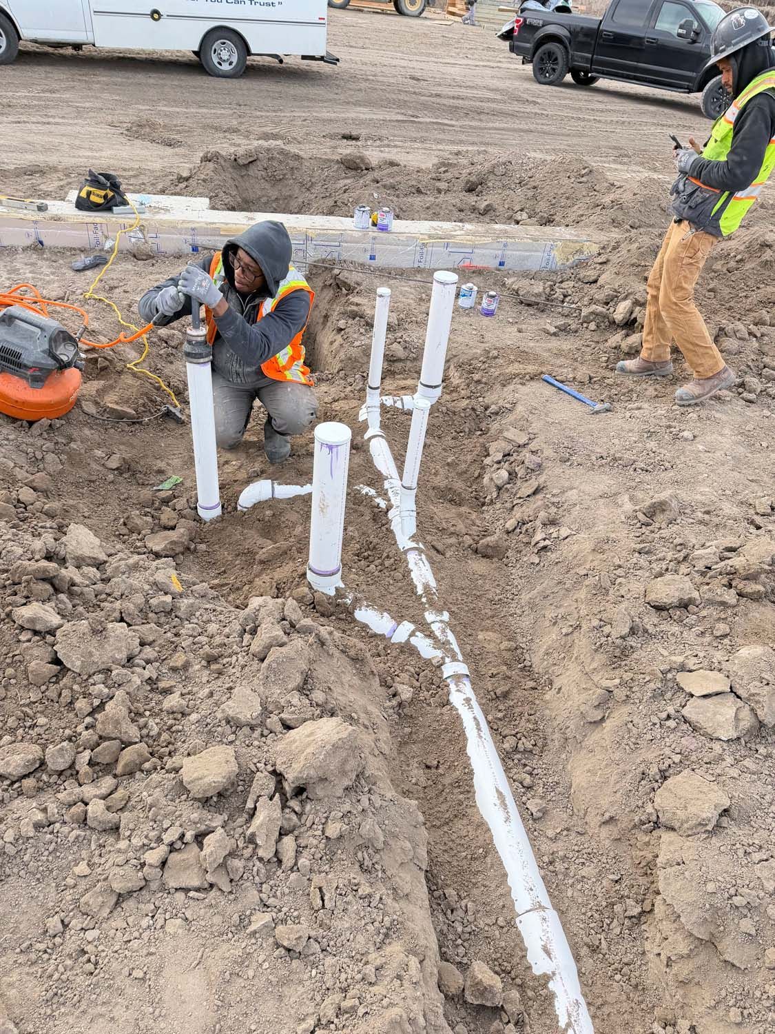 Workers installing PVC plumbing pipes in a trench at a construction site.