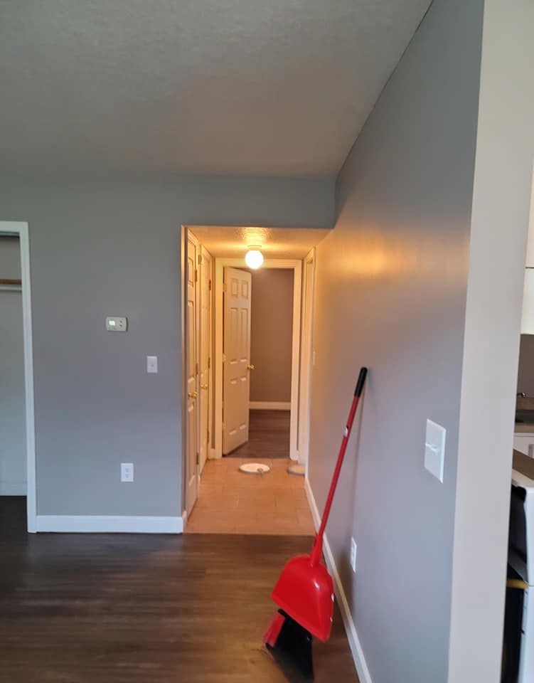 A red broom is sitting in a hallway next to a door.